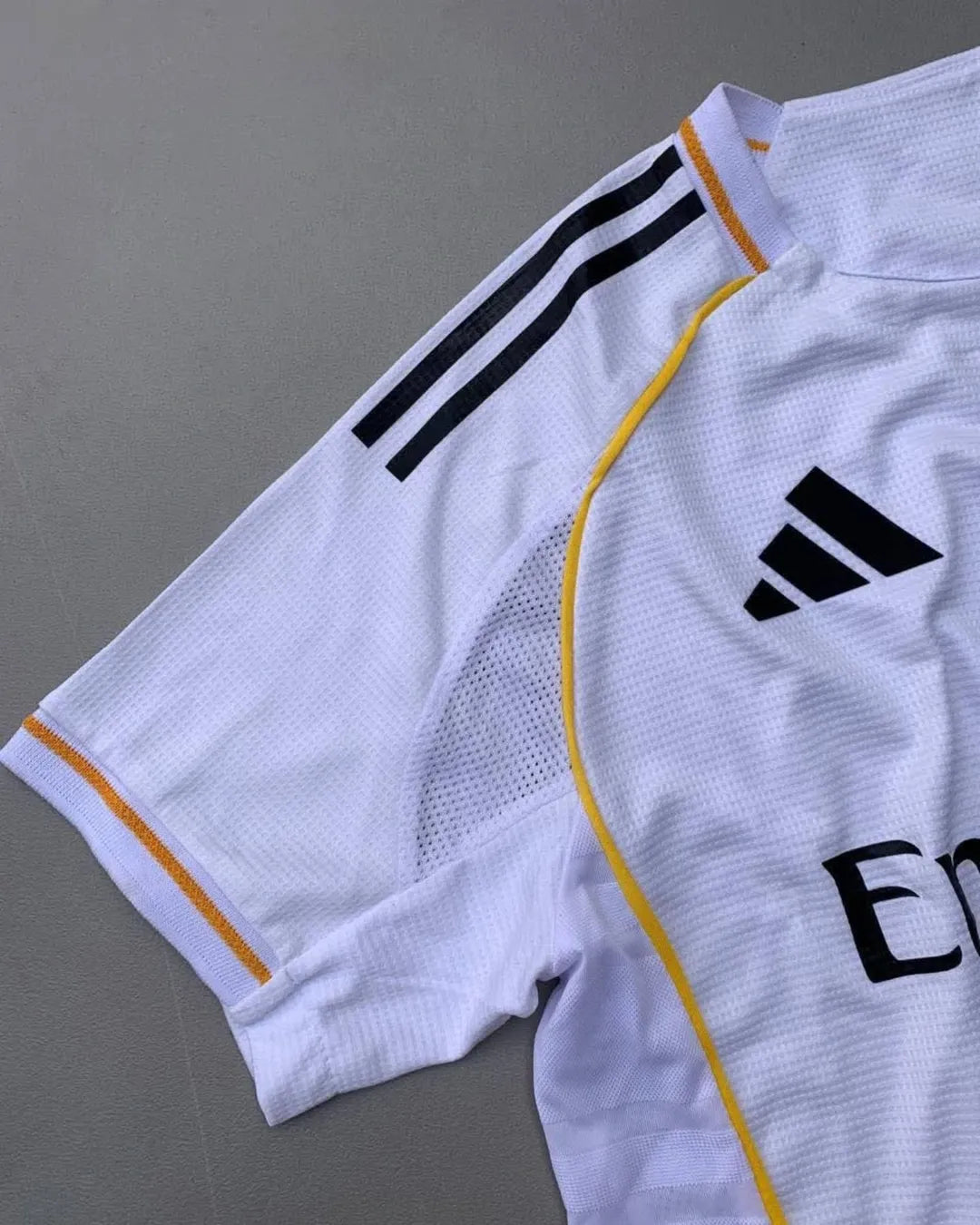 Real Madrid 2025/26 home jersey with classic white design, black adidas stripes, golden-yellow trim, Emirates Fly Better sponsor, and embroidered club crest – official fan and player kit