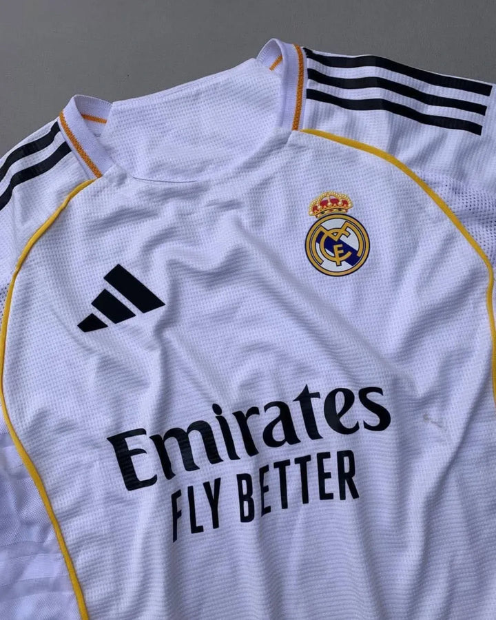 Real Madrid 2025/26 home jersey with classic white design, black adidas stripes, golden-yellow trim, Emirates Fly Better sponsor, and embroidered club crest – official fan and player kit